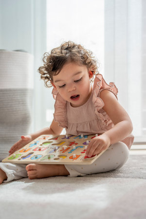 Vertical photograph of a little girl playing on the carpet in her room with a wooden puzzle, sustainable materials, learning and child development. practice fine motor skills. cognitive development.の写真素材