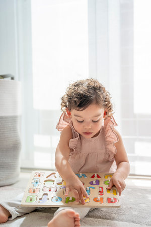 Vertical photograph of a little girl playing in her room with a wooden letter puzzle. Fun and...