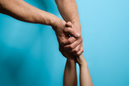 Hands of a father interlocking with his daughter`s hands over a blue background.の写真素材