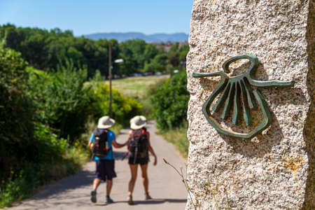 Pilgrims on the route of the Camino de Santiago (Way of Saint James) passing next to the scallop shell that marks the wayの写真素材