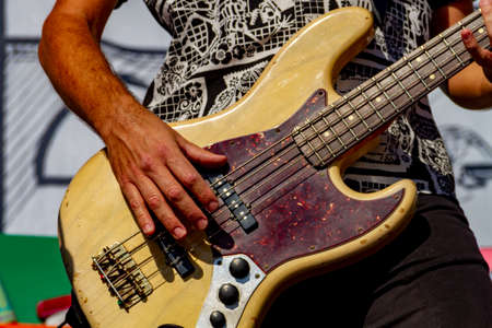 An unidentified musician plays an electric bass guitar during a concert in bright sunlightの写真素材