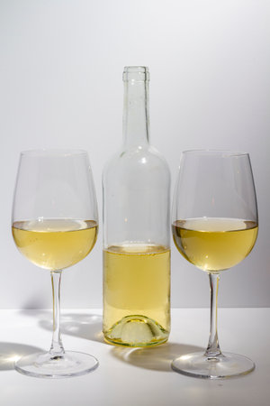 Transparent bottle with white wine inside and two glasses with white wine on a white background.の写真素材