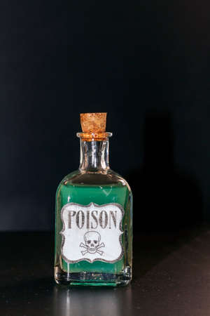 Concept of toxic thing. Transparent bottle with green liquid simulating poison. The label reads poison along with a skull and two tibiasの写真素材