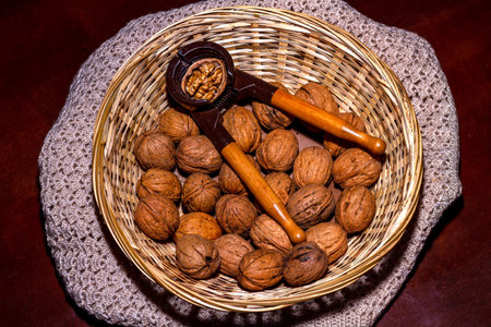 Wicker basket with walnuts on crocheted tablecloth. Inside are walnuts with a nutcracker that has a...