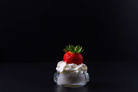 A strawberry partially dipped in a bowl containing whipped cream. All with a black background.の写真素材