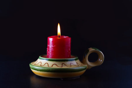 A lit red candle in a yellow and green ceramic candlestick. Cocept of hope.の写真素材