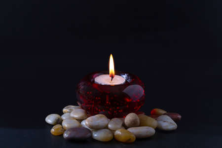 Mourning or prayer concept. Burning candle in a round red candlestick with colored stones surrounding it. All this on a black background.の写真素材