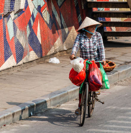 Unidentified woman rides bicycle along a street of Hanoi, Vietnamのeditorial素材
