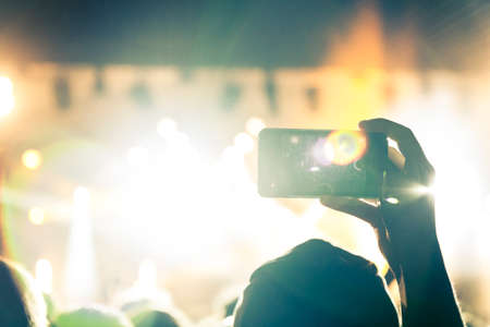 Multi colored concert crowd inside a venue during a live band show performance on stage.の写真素材