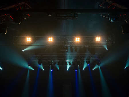 Photo of a concert hall with people silhouettes clapping in front of a big stage lit by spotlights. Shot is taken from concert crowd point of view.の写真素材