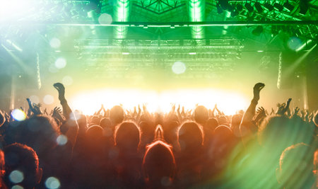 Concert stage shot from inside a concert hall with many people silhouettes attending the show,...