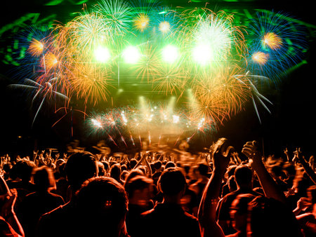 Multi colored concert crowd inside a venue during a live band show performance on stage.