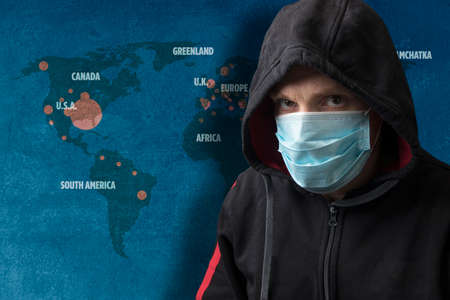 Portrait of a cloaked man wearing a surgical respiratory mask against coronavirus COVID-19 viral infection. Background is a map of the epidemic.の写真素材