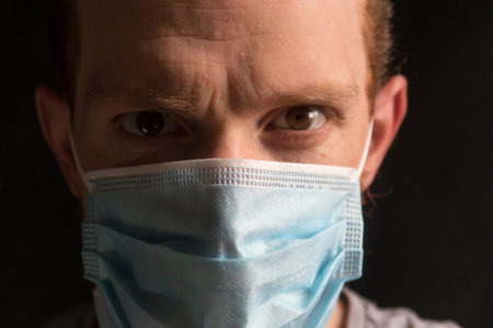 Close up selfie of a redheaded man wearing a surgical respiratory mask against COVID-19 coronavirus,...