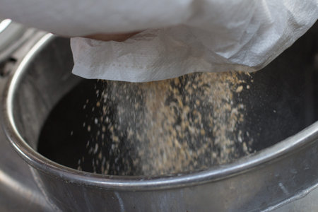 Detail of pouring beer malt into an industrial boiler, inside a brewery. Malt is blurred because of...