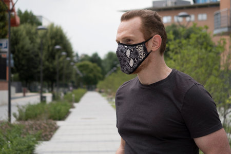 Close-up portrait of a redhead man wearing a respiratory mask against COVID-19 coronavirus,...