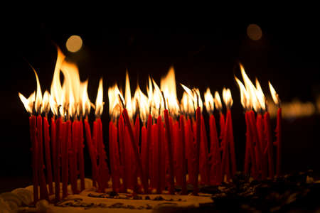 Burning candles on a birthday cake in a dark room, no people are visible.の写真素材