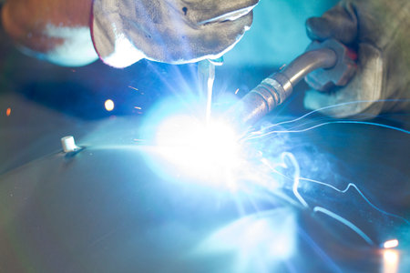 Close up on a welding machine in action, handheld by a worker wearing protective gloves.
