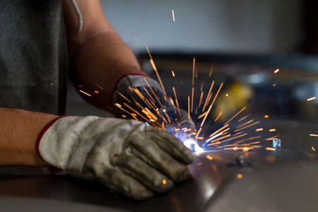 Close up on a welding machine in action, handheld by a worker wearing protective gloves.の写真素材
