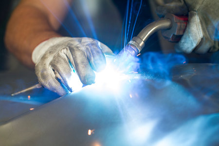 Close up on a welding machine in action, handheld by a worker wearing protective gloves.