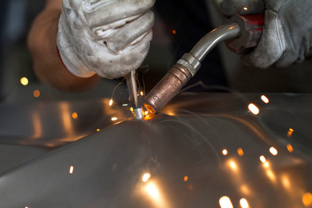 Close up on a welding machine in action, handheld by a worker wearing protective gloves.