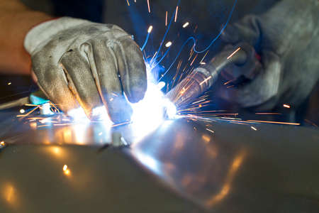 Close up on a welding machine in action, handheld by a worker wearing protective gloves.の写真素材