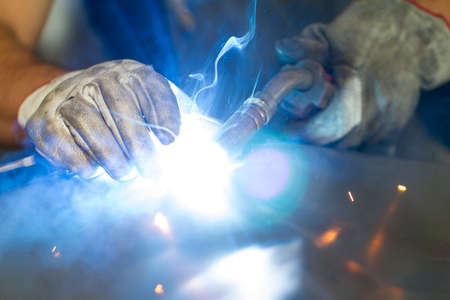 Close up on a welding machine in action, handheld by a worker wearing protective gloves.の写真素材