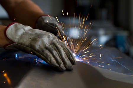 Close up on a welding machine in action, handheld by a worker wearing protective gloves.の写真素材