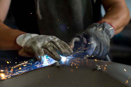 Close up on a welding machine in action, handheld by a worker wearing protective gloves.の写真素材