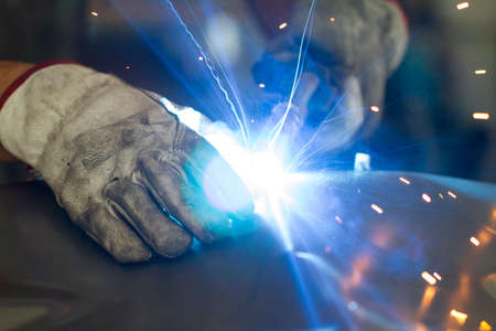 Close up on a welding machine in action, handheld by a worker wearing protective gloves.の写真素材