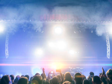Concert crowd in front of a brightly lit stage; in the background clapping hands and lights are visibleの写真素材