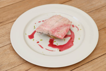 A piece of tuna steak on a white plate with a berry sauce