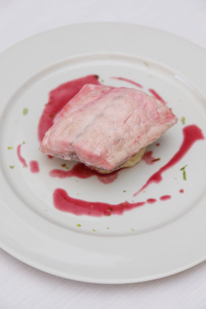 A piece of pork with berry sauce on a white plate.