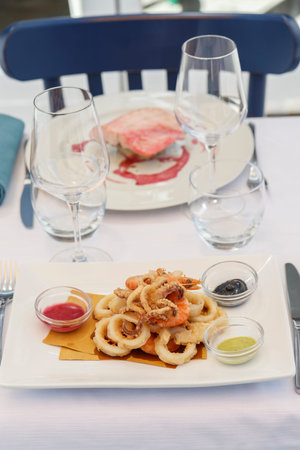 fried squid rings on a white plate and two glasses of red wine
