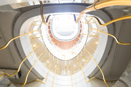 Interior of a modern shopping mall with a spiral staircase and gold lightsの写真素材