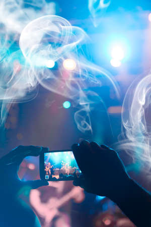 Image shot during a music festival. Light comes from a stage with a band show, people silhouettes are visible in front of it.の写真素材
