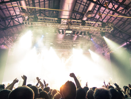 Crowd at a concert in front of bright stage lights with hands raisedの写真素材