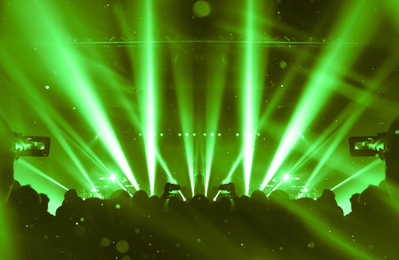 Image shot during a music festival. Light comes from a stage with a band show, people silhouettes are visible in front of it.の写真素材