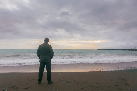 Solitary man standing by the seaside and staring in the distance. He's wearing a military outfit and...