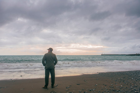 Solitary man standing by the seaside and staring in the distance. He's wearing a military outfit and...