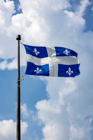 Flag of Quebec waving in the wind against blue sky with white clouds