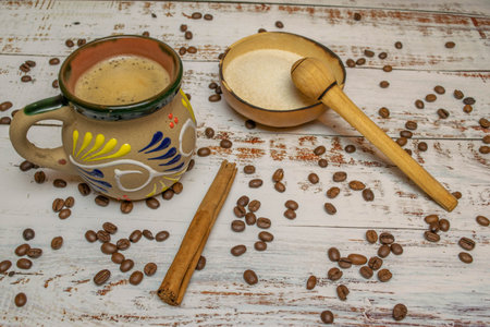Mexican coffee with cinnamon in cup with Mexican decoration on white wooden table with organic coffee beans and natural bowl with milk and wooden spoonの写真素材