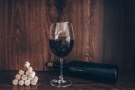 photograph of corks and glass of red wine and bottle of wine all on wooden backgroundの写真素材