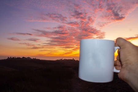 pov photo of hand having a cup of coffee in the sunset of a red skyの写真素材