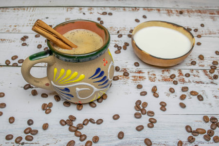 Mexican coffee with cinnamon in cup with Mexican decoration on white wooden table with organic coffee beans and natural bowl with milk and wooden spoonの写真素材