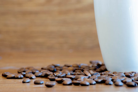 delicious organic and roasted coffee beans on wooden table next to white cup