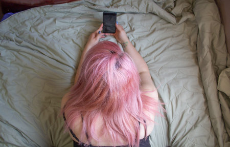 Pink haired woman lying on the bed. using old camera