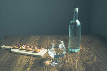 glass and bottle with crystalline liquor like vodka, tequila or mezcal. accompanied by spicy oranges