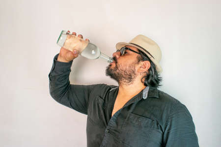 man with a Latino look drinking from a bottle of clear liquor, like crystal tequila, vodka or mezcalの写真素材