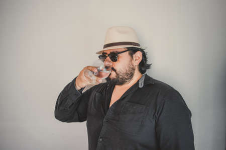 man with a Latin look drinking from the glass with clear liquor, like crystal tequila, vodka or mezcalの写真素材